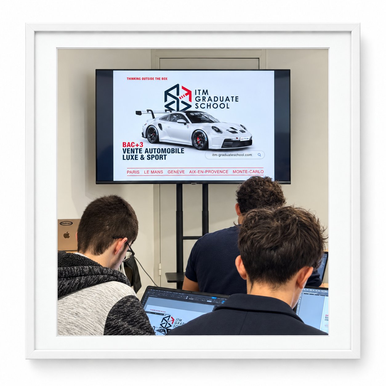 Étudiants d’ITM School travaillant sur ordinateur devant une présentation de l’école, dans une photographie sous cadre blanc.