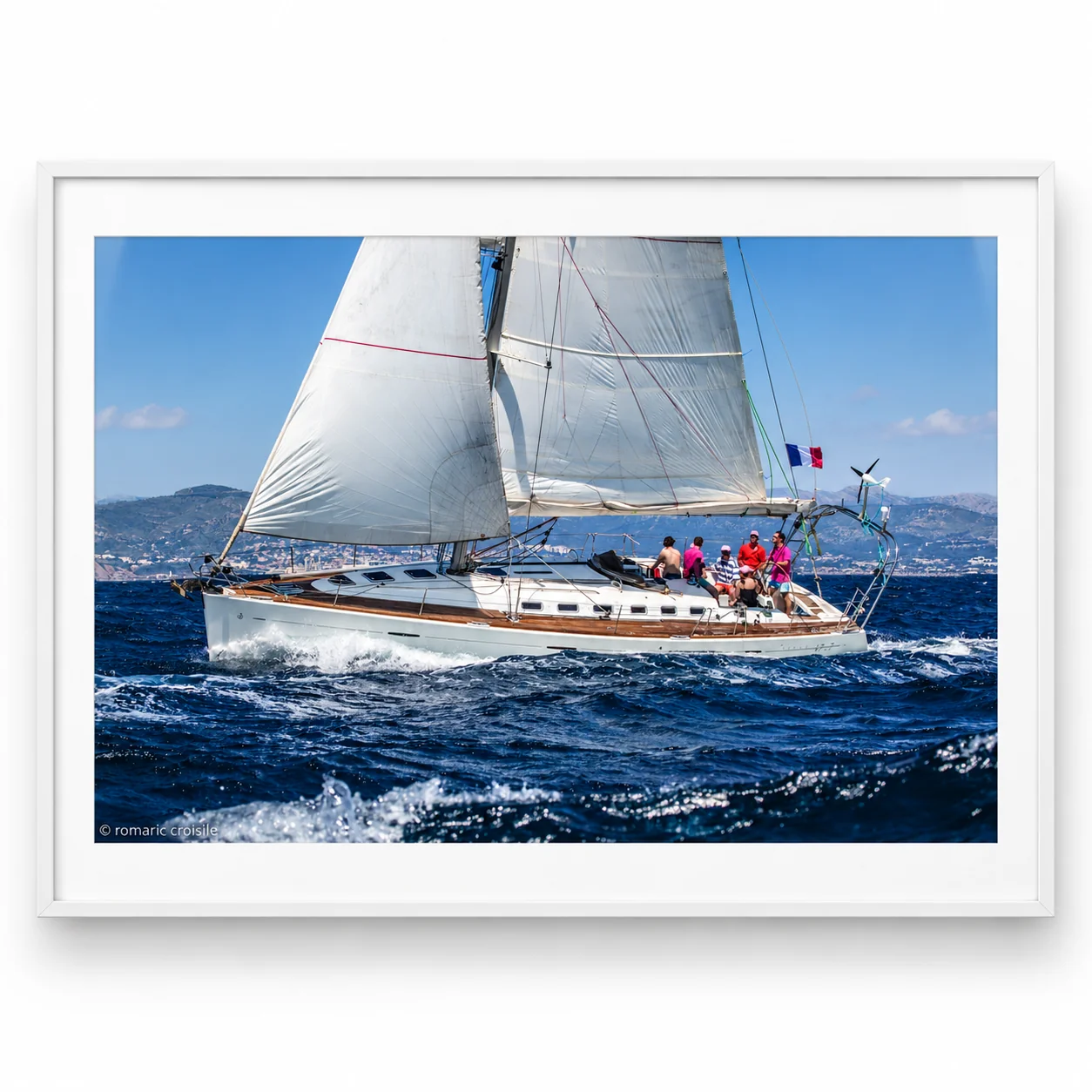 Voilier First 47.7 naviguant en mer avec des passagers à bord, présenté sous verre dans un cadre blanc.