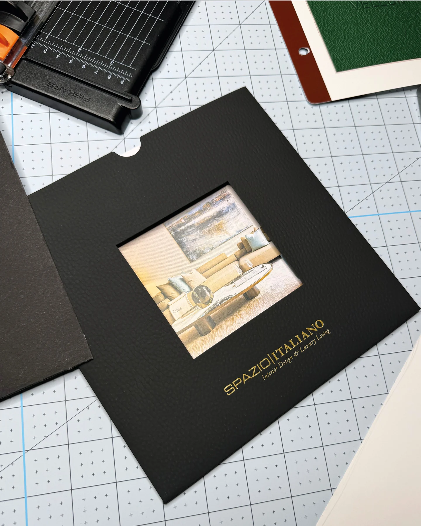 Pochette noire Spazio Italiano avec fenêtre découpée laissant apparaître un salon, photographiée sur une table de travail.